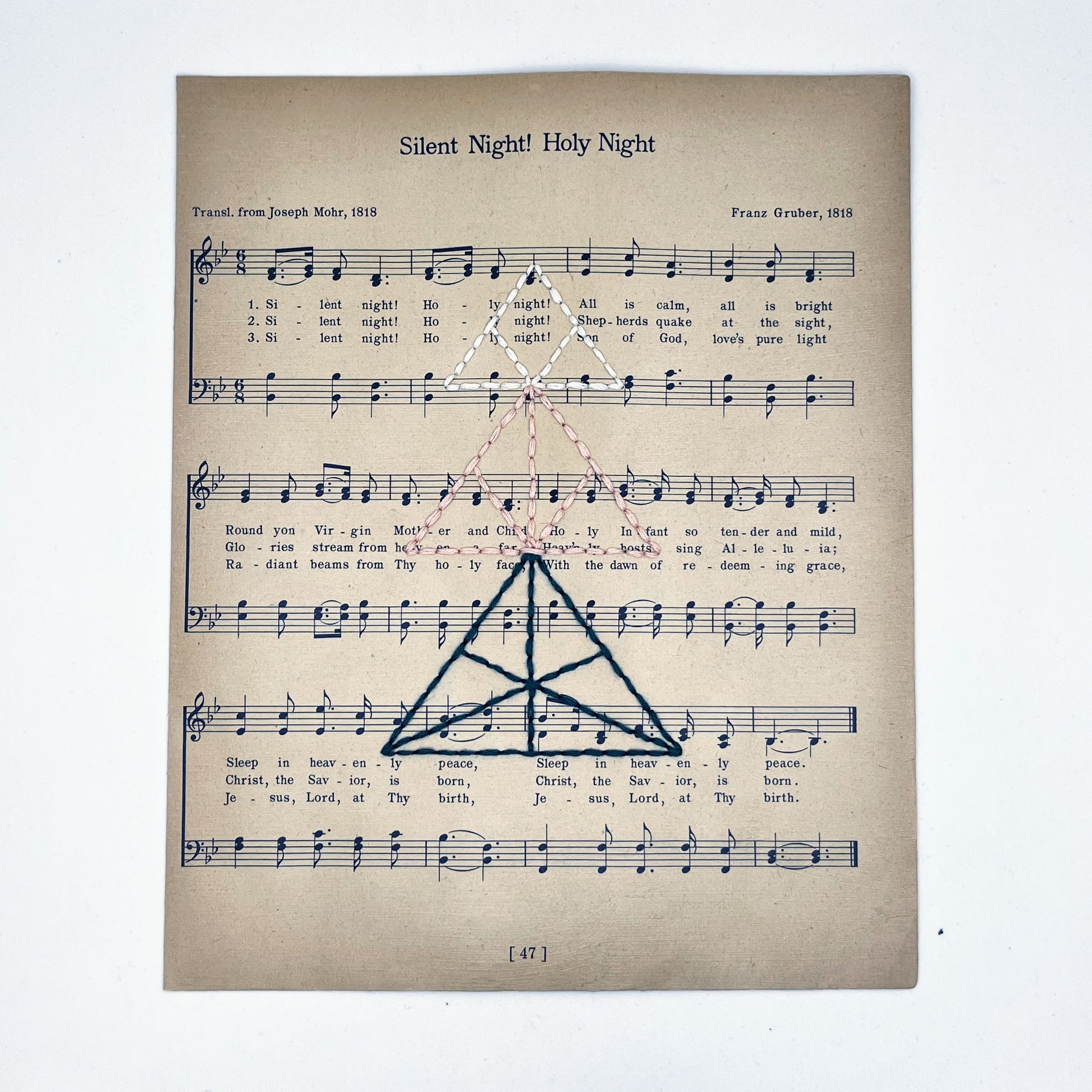 sheet music from the Christmas song "Silent Night", hand stitched over with a Christmas tree made from triangles, in green, peach and ivory thread