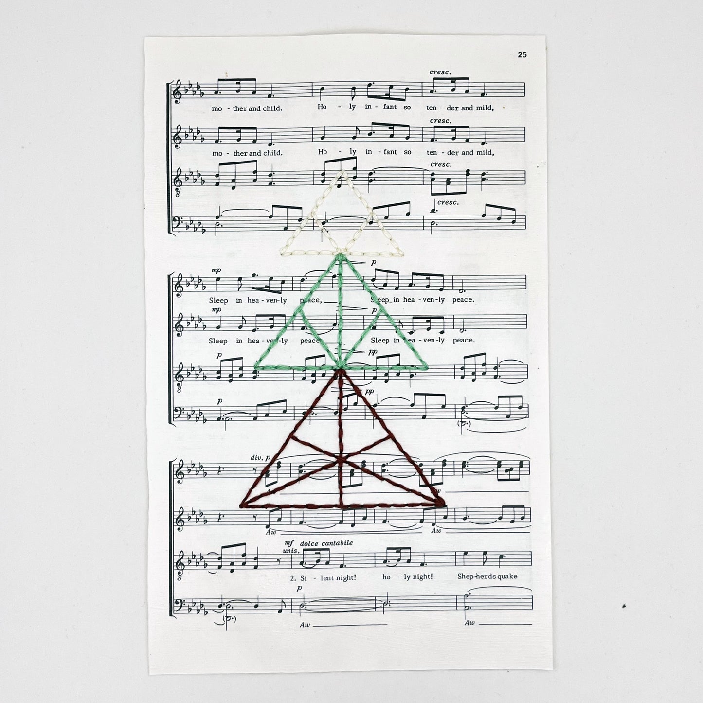 sheet music from the Christmas song "Silent Night", hand stitched over with a Christmas tree made from triangles, in red, green and ivory thread