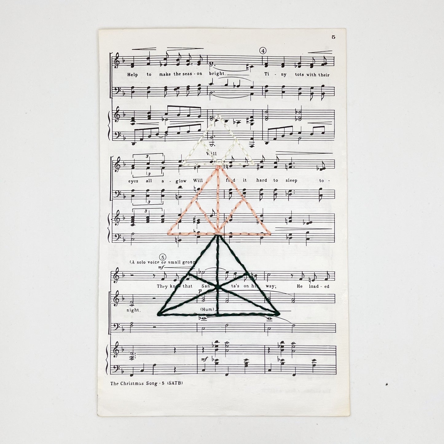 sheet music from "The Christmas Song", hand stitched over with a Christmas tree made from triangles, in green, peach and ivory thread