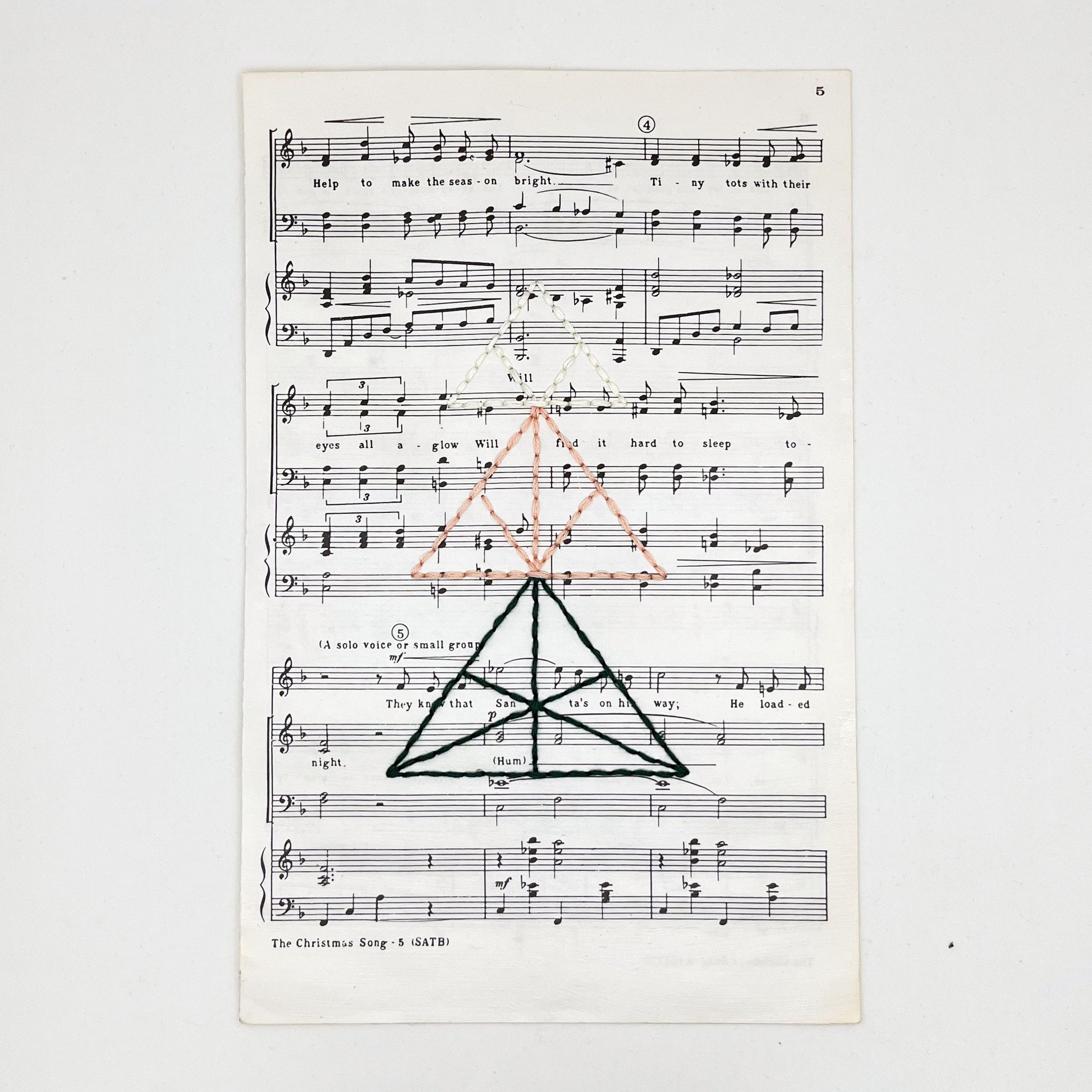sheet music from "The Christmas Song", hand stitched over with a Christmas tree made from triangles, in green, peach and ivory thread